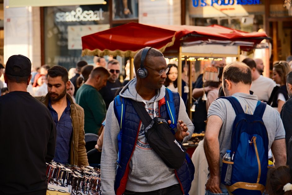 A person wearing a modern, anti-theft backpack walking through a vibrant, crowded market, with diverse faces and colorful stalls in the background.