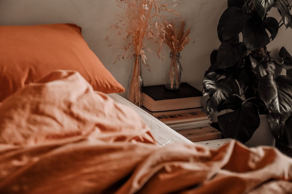 A bedroom featuring soft, high-quality bedding, a plant on the nightstand, and blackout curtains, illustrating comfort-focused textile upgrades.