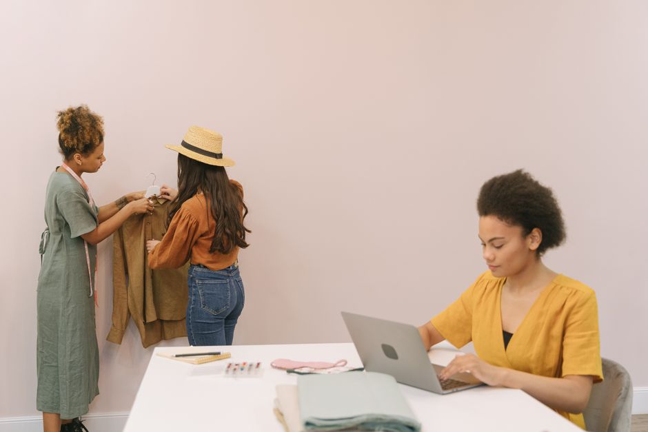 Three professional women in a modern office environment, dressed in business casual easy workwear outfits, engaging in a discussion.