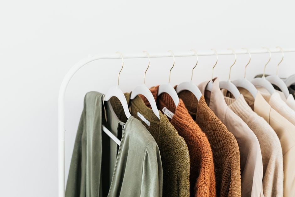 A neatly organized capsule wardrobe with neutral-toned workwear staples like tailored blazers, trousers, skirts, and classic shirts on hangers.
