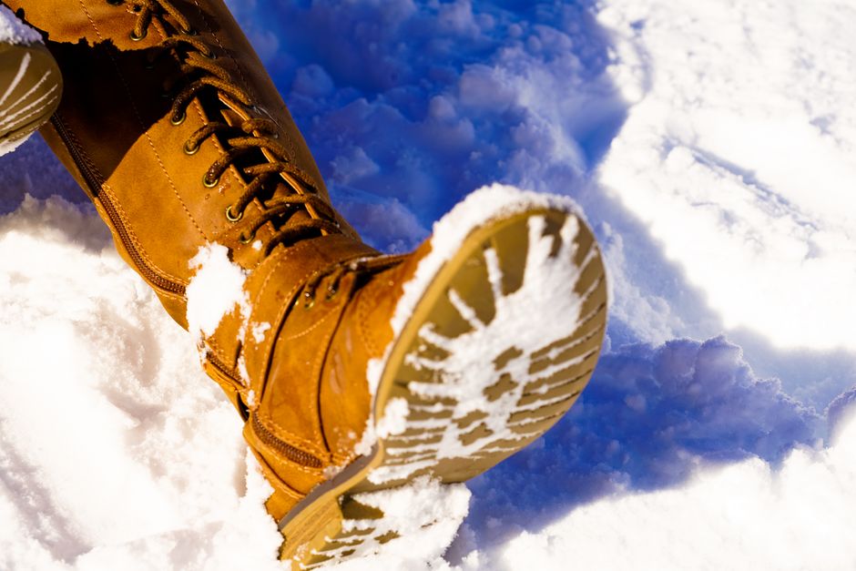 Detailed shot of the robust rubber outsole of a winter boot, showing deep, multi-directional lugs designed for superior grip on a patch of ice and snow.