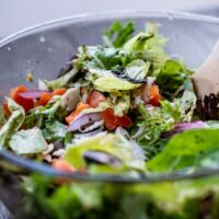A vibrant, colorful no-cook salad bowl filled with fresh greens, cherry tomatoes, cucumber, chickpeas, feta, and olives, with a light vinaigrette.