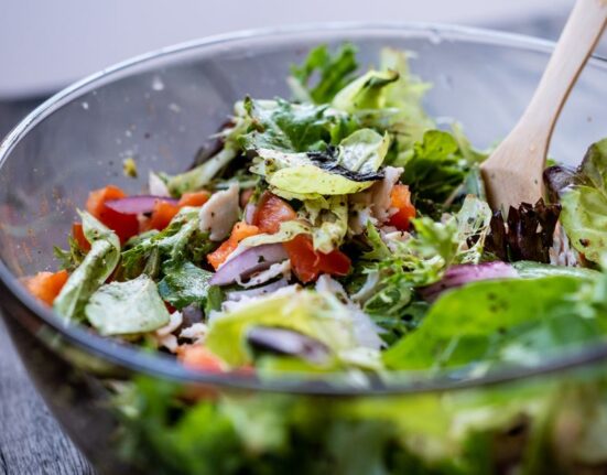 A vibrant, colorful no-cook salad bowl filled with fresh greens, cherry tomatoes, cucumber, chickpeas, feta, and olives, with a light vinaigrette.