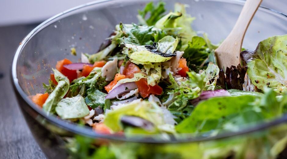 A vibrant, colorful no-cook salad bowl filled with fresh greens, cherry tomatoes, cucumber, chickpeas, feta, and olives, with a light vinaigrette.