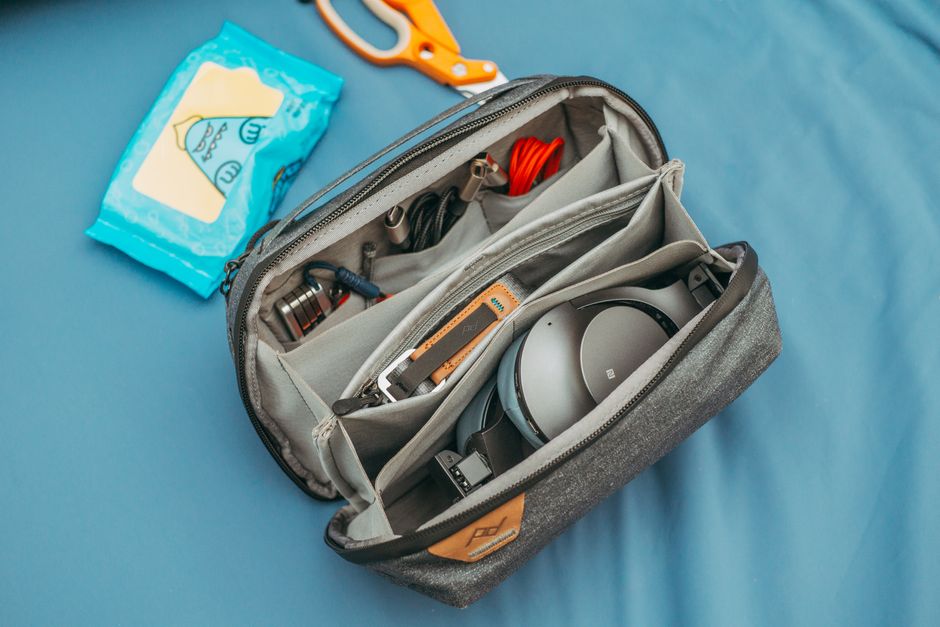 Various compact and useful everyday products for travel, neatly arranged: a solid shampoo bar, a universal travel adapter, a rolled microfiber towel, and a reusable water bottle, all within a small backpack.