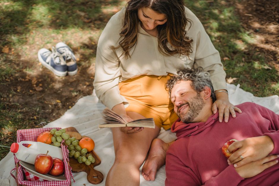 A happy couple enjoying a picnic on a sunny day in a picturesque city park, with sandwiches and drinks, demonstrating a budget-friendly activity during a trip.