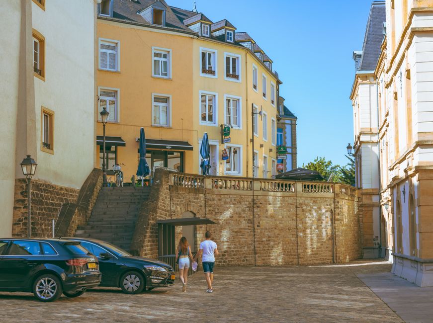 A couple walking hand-in-hand down a narrow, historic street in an old European city, looking at traditional buildings.