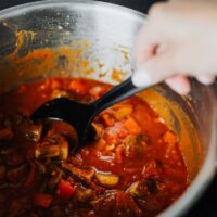 A steaming, rich beef and vegetable stew in a large Dutch oven on a rustic wooden table, with cozy lighting and a warm ambiance.
