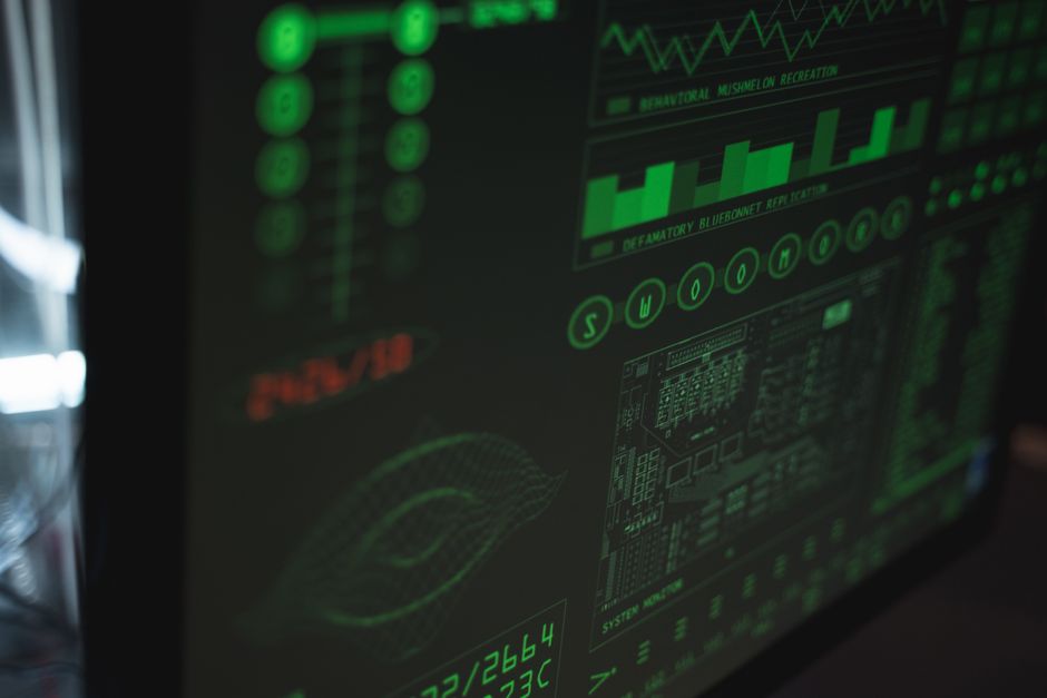 Close-up of a computer screen displaying a cybersecurity dashboard with charts and threat alerts, while a small team works in the softly blurred background.