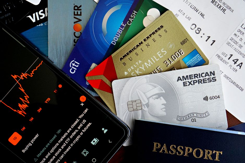 An assortment of credit and debit cards from different banks, with various international currency notes like Euros, Dollars, and Pounds scattered around them, symbolizing options for travel payments.