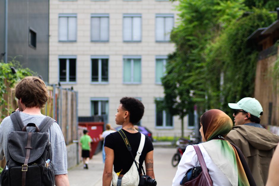 A diverse group of people walking confidently down a well-lit, bustling European city street at dusk, showcasing varied architecture and activity.