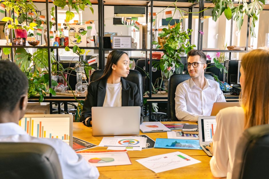 Diverse professionals from a small agency are working on laptops, with a background displaying various data charts and a CRM workflow.