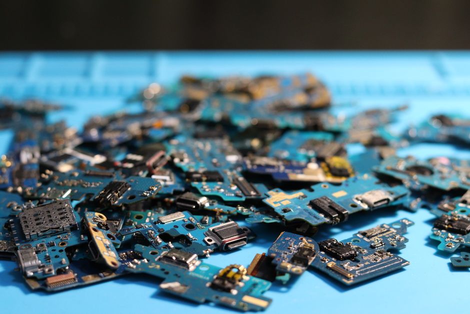 A close-up view of various circuit boards, wires, and electronic parts in a bin, ready for processing at an e-waste plant.
