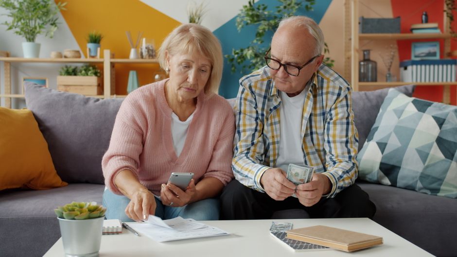 A family, including parents and a child, gathered around a tablet, looking at budgeting software or a spreadsheet, with a small pile of coins and a piggy bank nearby, representing financial planning.