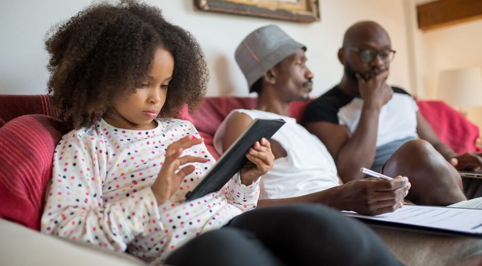 A diverse family, including parents and children, gathered around a kitchen island, interacting with a smart home tablet to manage their daily schedule.