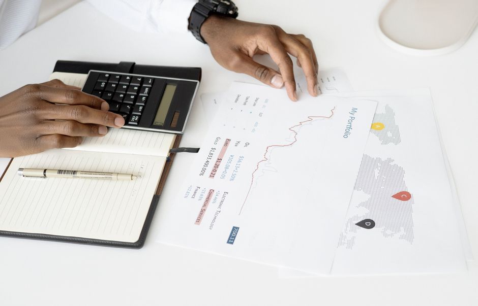 A person's hands working on a detailed financial spreadsheet with a calculator and coffee, representing diligent budgeting.