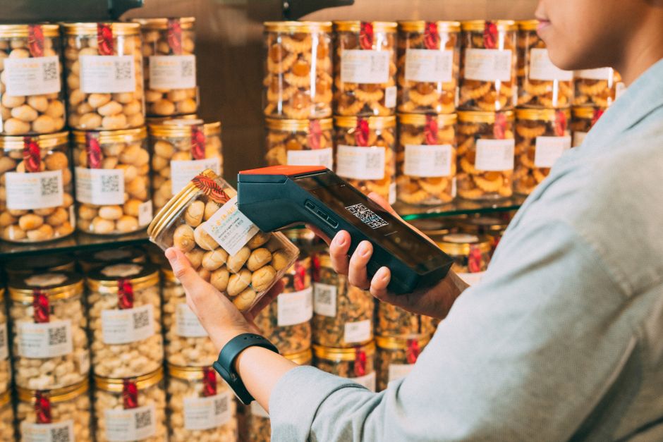 A close-up of a person's hand holding a packaged food item, with their other hand pointing to the nutrition label, indicating careful review.