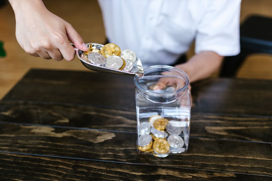 A hand dropping a coin into a glass jar labeled 'SAVINGS', illustrating the process of building an emergency fund or saving goals.