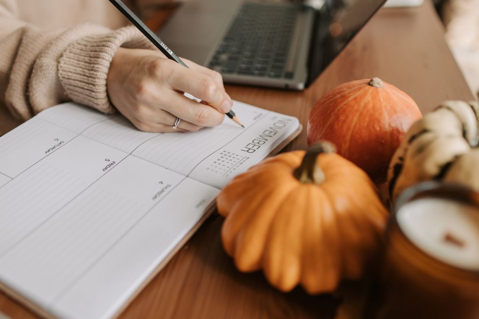 A close-up of a hand writing entries into a personal finance planner, with a laptop displaying a budgeting spreadsheet in the background, illustrating active tracking of expenses.