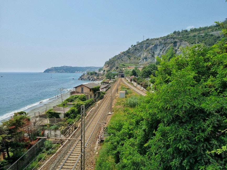 Regional train winding along the Italian Ligurian coast, with colorful houses of Cinque Terre villages visible by the sea.