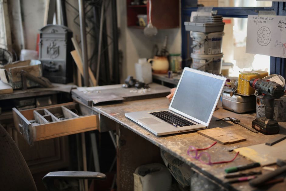 Close-up of a technician's hands working on the internal components of an open laptop, surrounded by tools and spare parts.