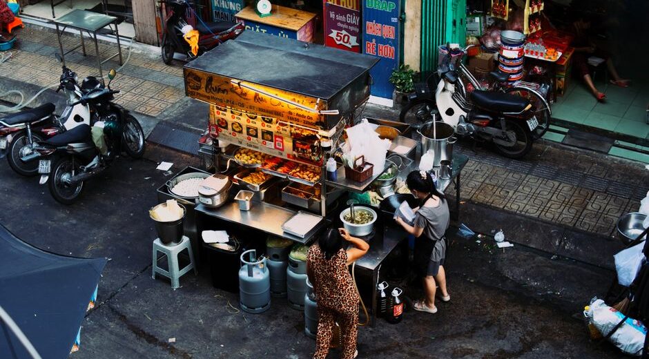 A bustling local market with fresh produce, cheese, and various food stalls, showing people interacting with vendors.