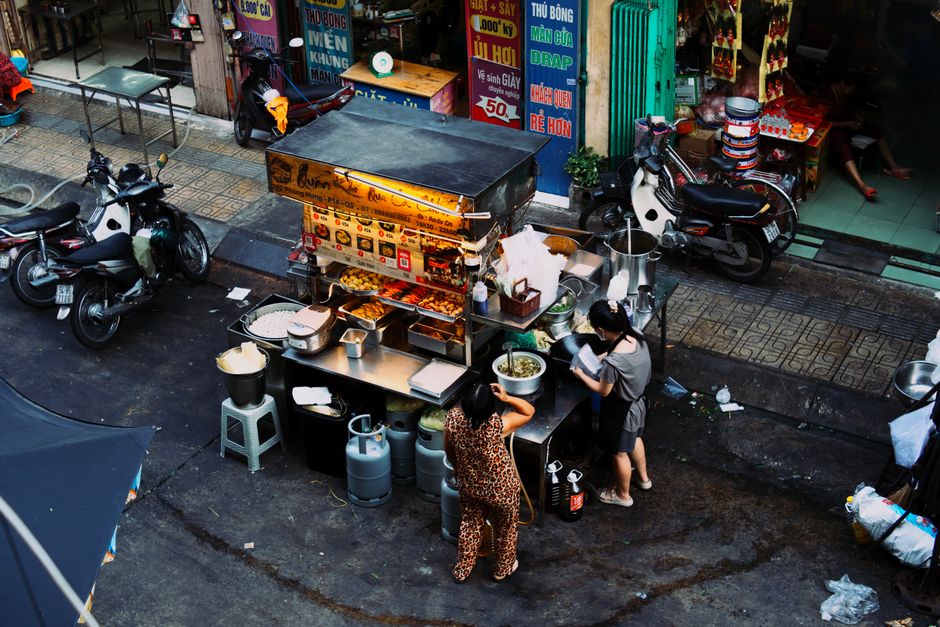 A bustling local market with fresh produce, cheese, and various food stalls, showing people interacting with vendors.