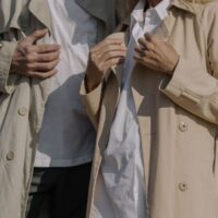 A man in a city street expertly layering a beige trench coat over a blue suit, showcasing adaptable men's fashion for unpredictable weather.
