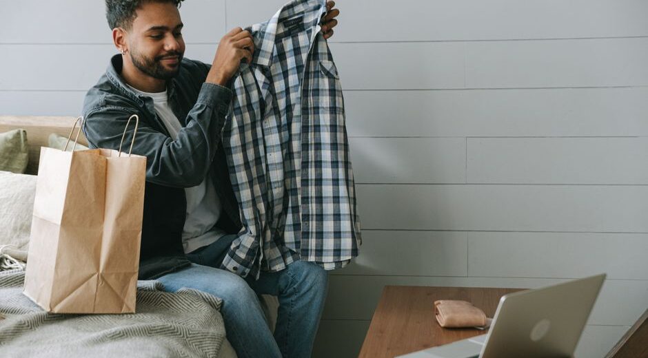 A man meticulously measuring the waist of a pair of jeans with a tape measure, preparing for an online purchase.