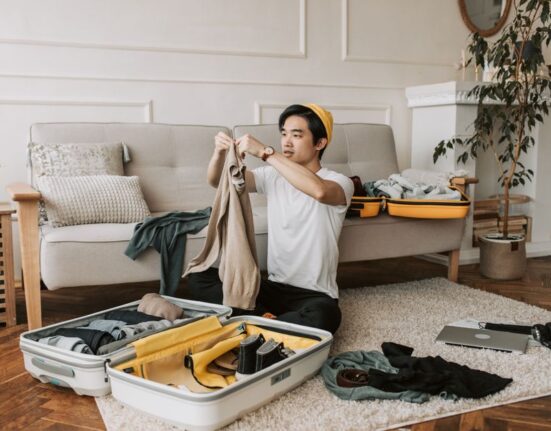 Man thoughtfully selecting clothes from a minimalist travel capsule wardrobe laid out on a bed, showing a few versatile items.