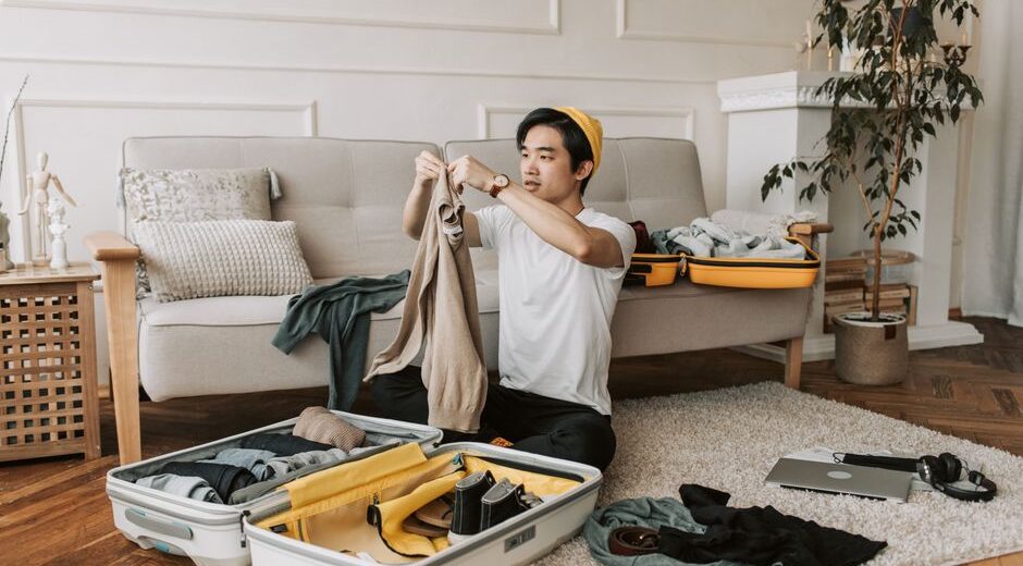 Man thoughtfully selecting clothes from a minimalist travel capsule wardrobe laid out on a bed, showing a few versatile items.
