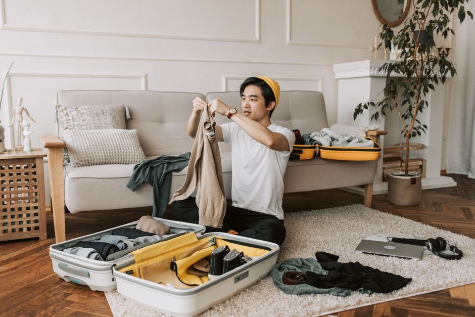Man thoughtfully selecting clothes from a minimalist travel capsule wardrobe laid out on a bed, showing a few versatile items.