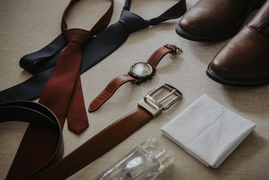 Overhead shot of a curated men's capsule wardrobe laid flat, featuring neutral-colored shirts, trousers, a blazer, and minimalist shoes.