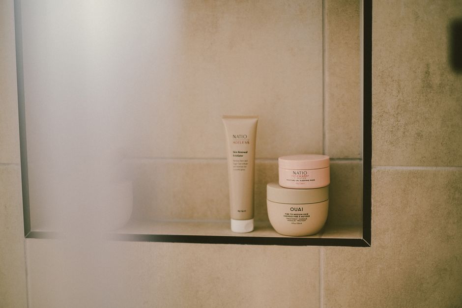 A clean, organized bathroom shelf displaying a few essential, low-maintenance beauty products: a cleanser, moisturizer, and sunscreen.