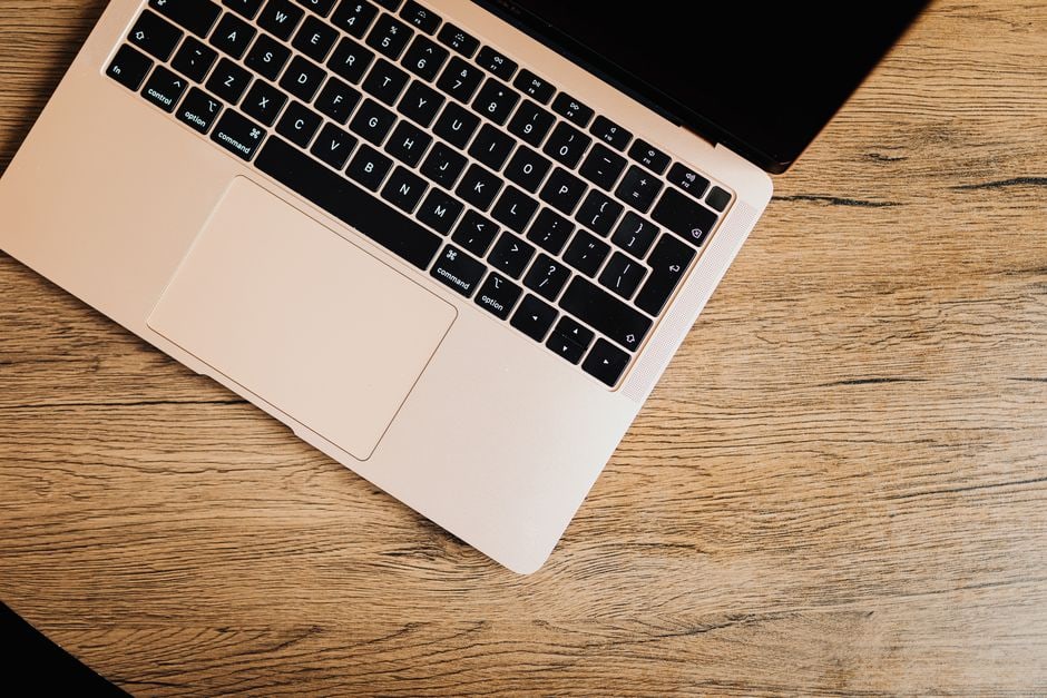 A brand new, thin, silver laptop open on a clean, minimalist desk in a modern home office setting, with a smartphone and a coffee cup nearby.