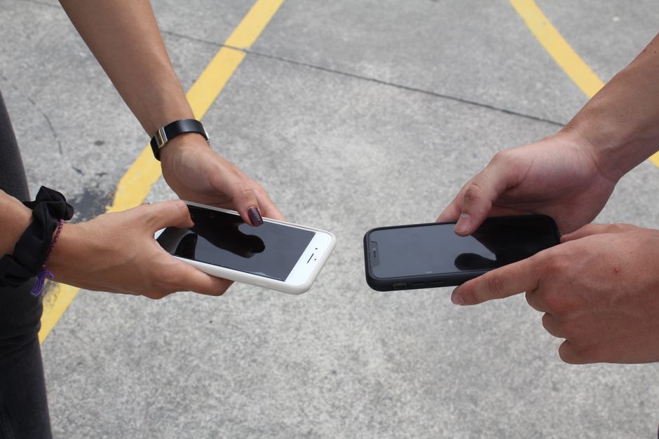 A person's hands holding a smartphone displaying an exchange rate comparison app, with blurred European city street in the background, illustrating the act of checking currency values.