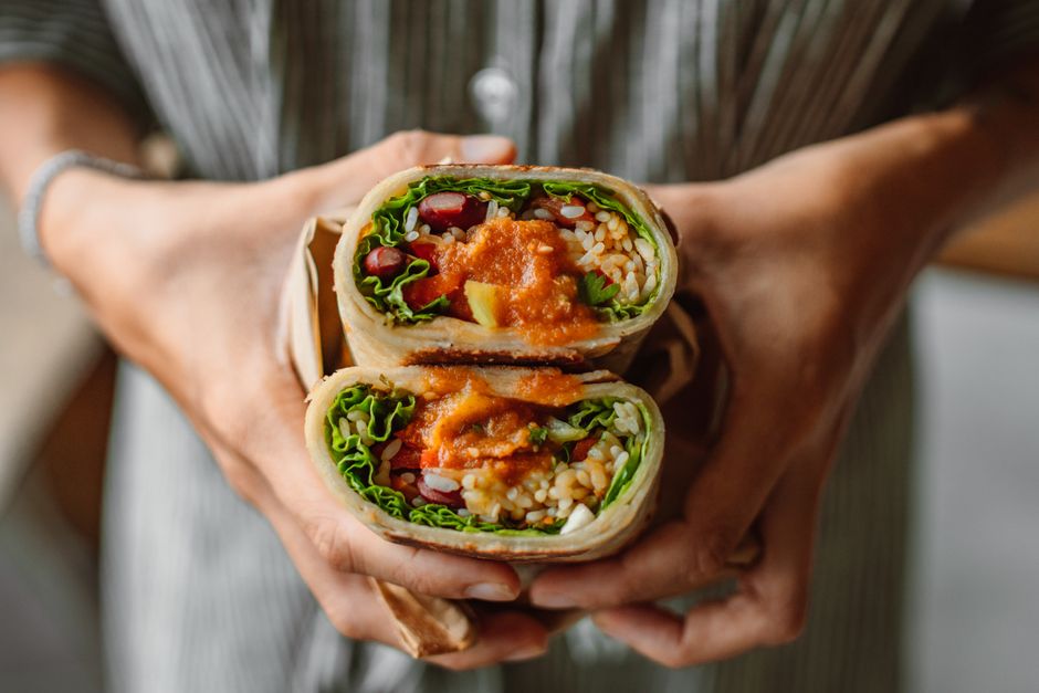 A person enjoying a refreshing, easy-to-make wrap outdoors on a sunny day, showcasing a convenient and healthy no-cook lunch option.