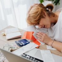A person looking stressed while reviewing financial documents and a laptop, symbolizing the challenge of overspending.