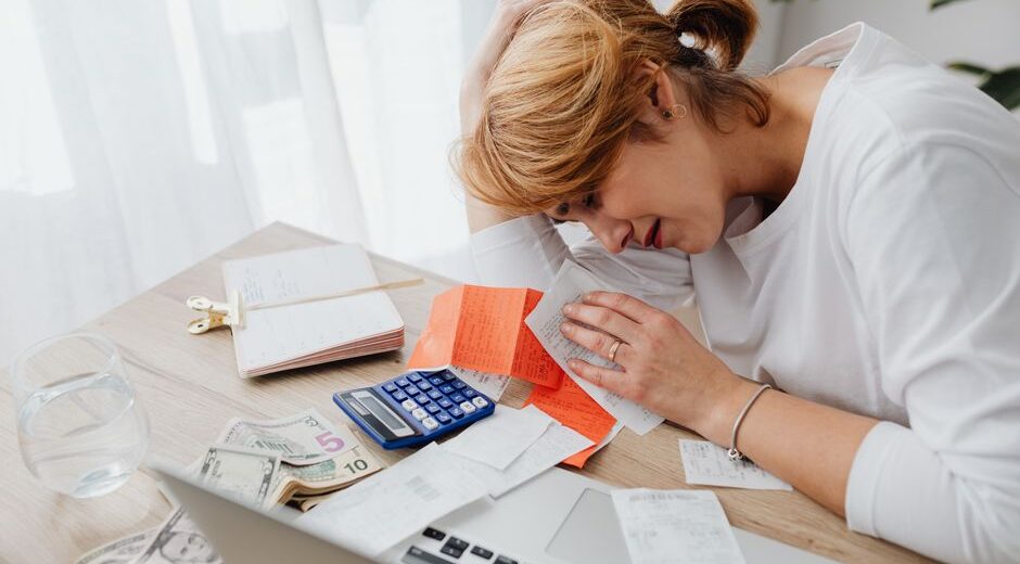 A person looking stressed while reviewing financial documents and a laptop, symbolizing the challenge of overspending.