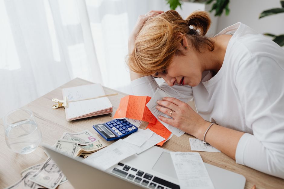 A person looking stressed while reviewing financial documents and a laptop, symbolizing the challenge of overspending.