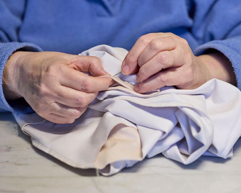 Close-up of hands carefully stitching a button onto a shirt, illustrating garment repair and longevity.