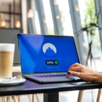 Person using a laptop at a cafe with an open public Wi-Fi connection, illustrating the need for a VPN for privacy and travel.
