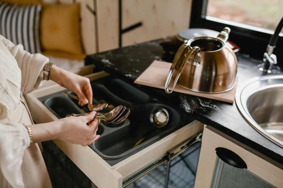 A person neatly arranging kitchen utensils in a bamboo drawer organizer, demonstrating home organization.