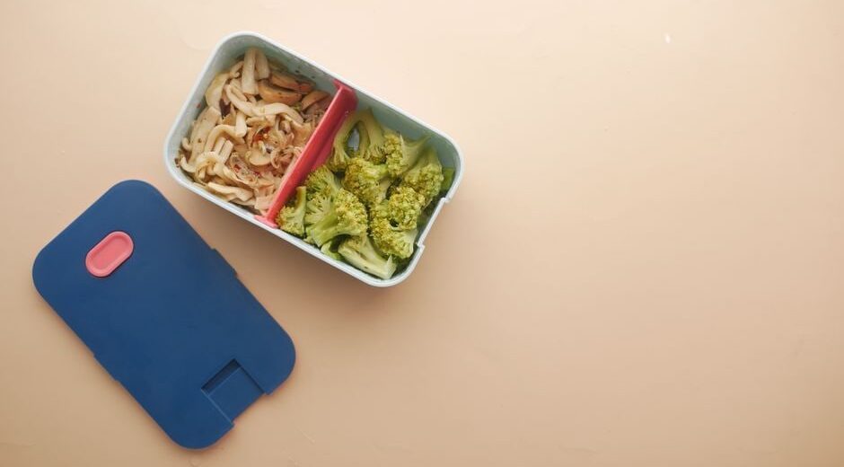 A person carefully packing colorful, healthy snacks into a bento box for an upcoming trip, showcasing meal prep.