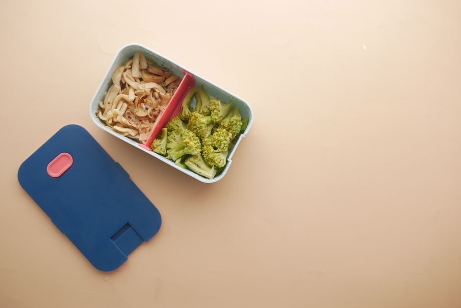 A person carefully packing colorful, healthy snacks into a bento box for an upcoming trip, showcasing meal prep.