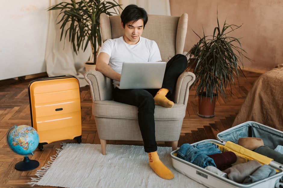 A person with a laptop open, looking at a map and a notebook, surrounded by travel guides and a cup of coffee, signifying meticulous planning for a trip.