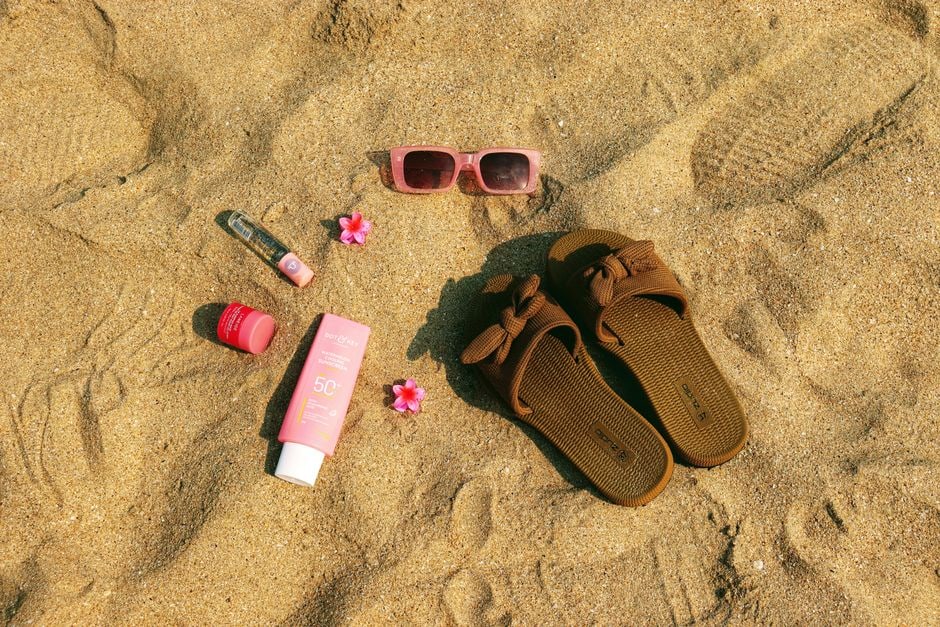A person gently patting a powder sunscreen stick over their cheek, protecting their skin while wearing light makeup on a sunny beach.