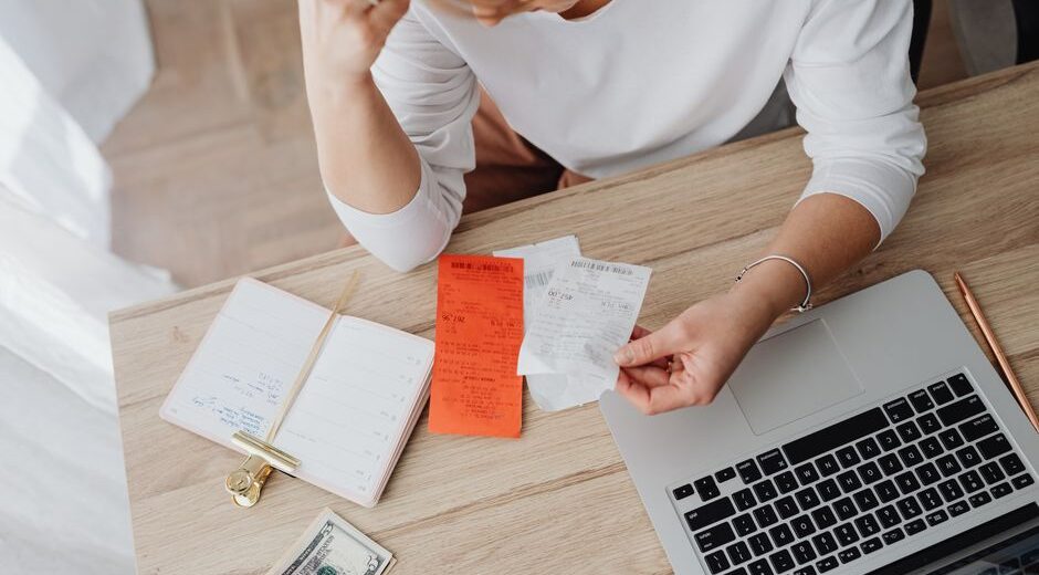 A person tracking expenses on a laptop, with a notebook and pen nearby, representing the first step in budgeting.