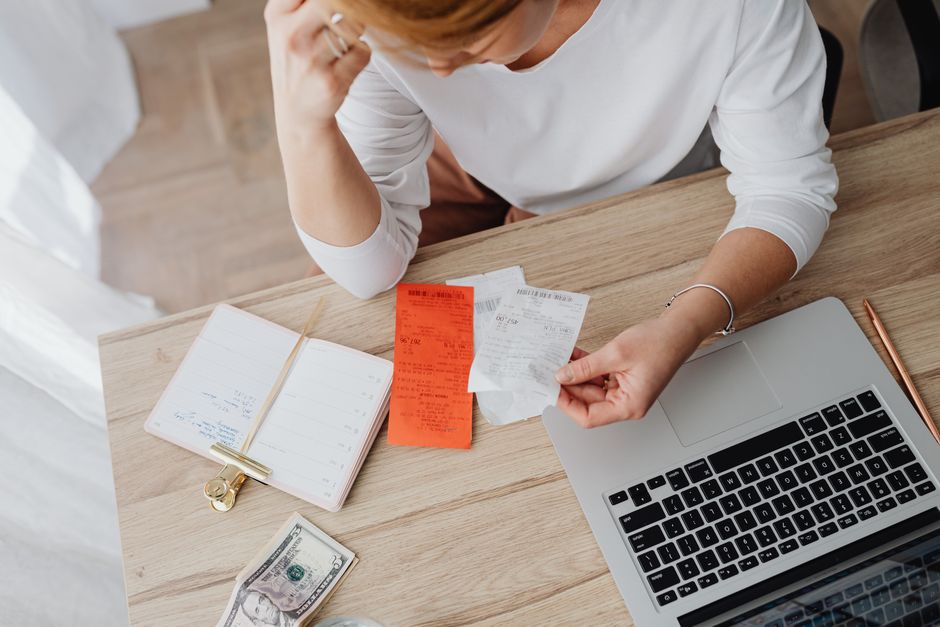 A person tracking expenses on a laptop, with a notebook and pen nearby, representing the first step in budgeting.