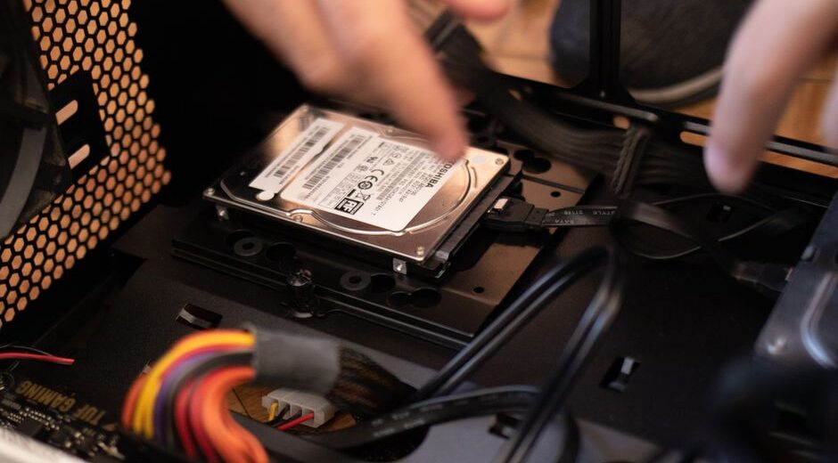 A close-up of a person installing a Solid-State Drive (SSD) into an open laptop, symbolizing a budget tech upgrade.